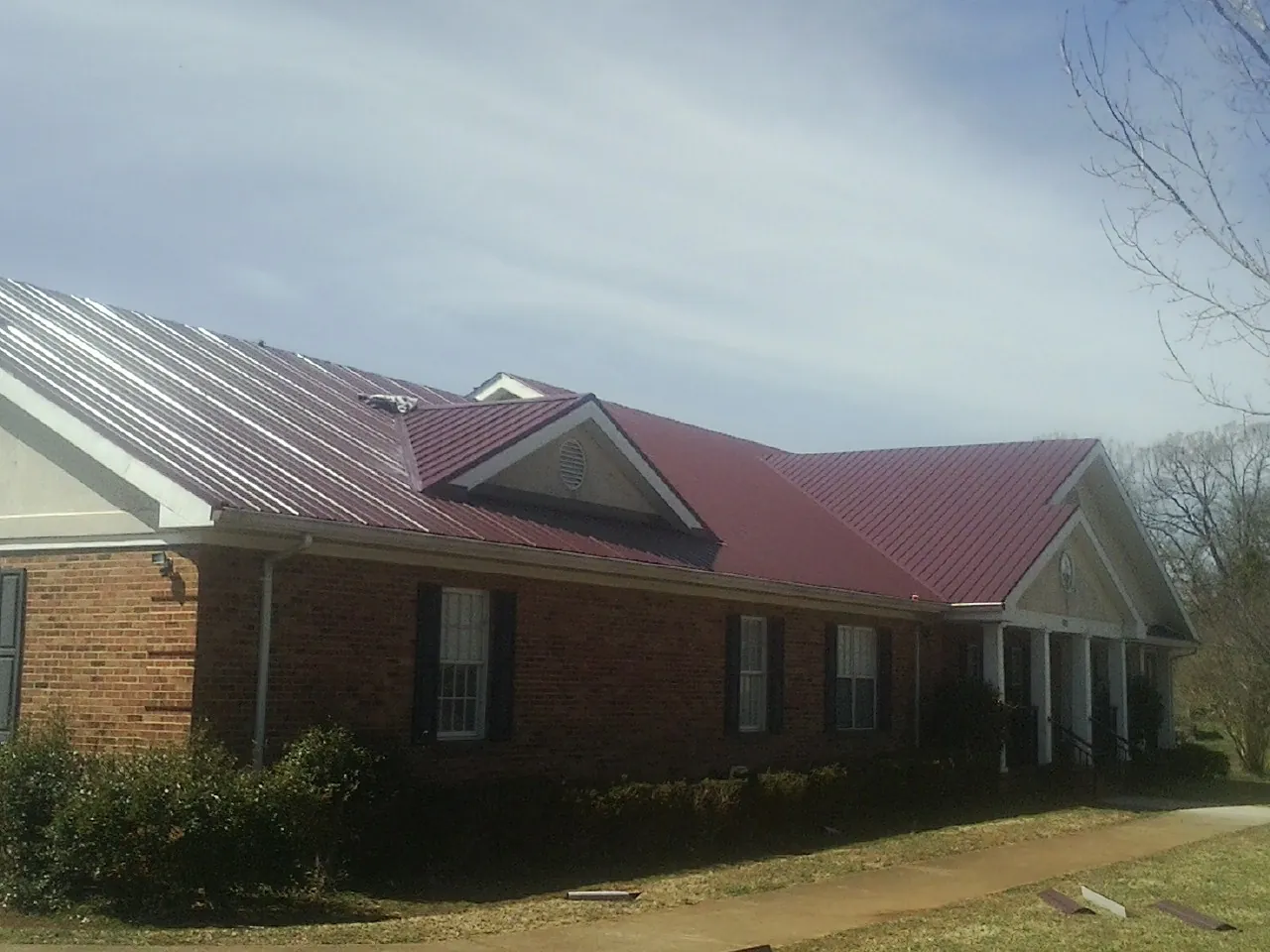 Red metal roof with gabled entries on a long brick building, from a Hail Damage Roof Repair job in Cedar Creek