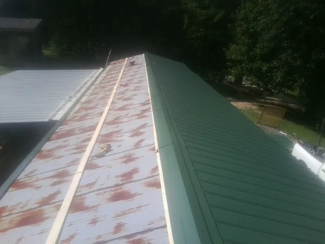 Old rusted panels beside newly installed green metal roofing — Wind Damage Roof Repair by Roofing Brothers in Cedar Creek