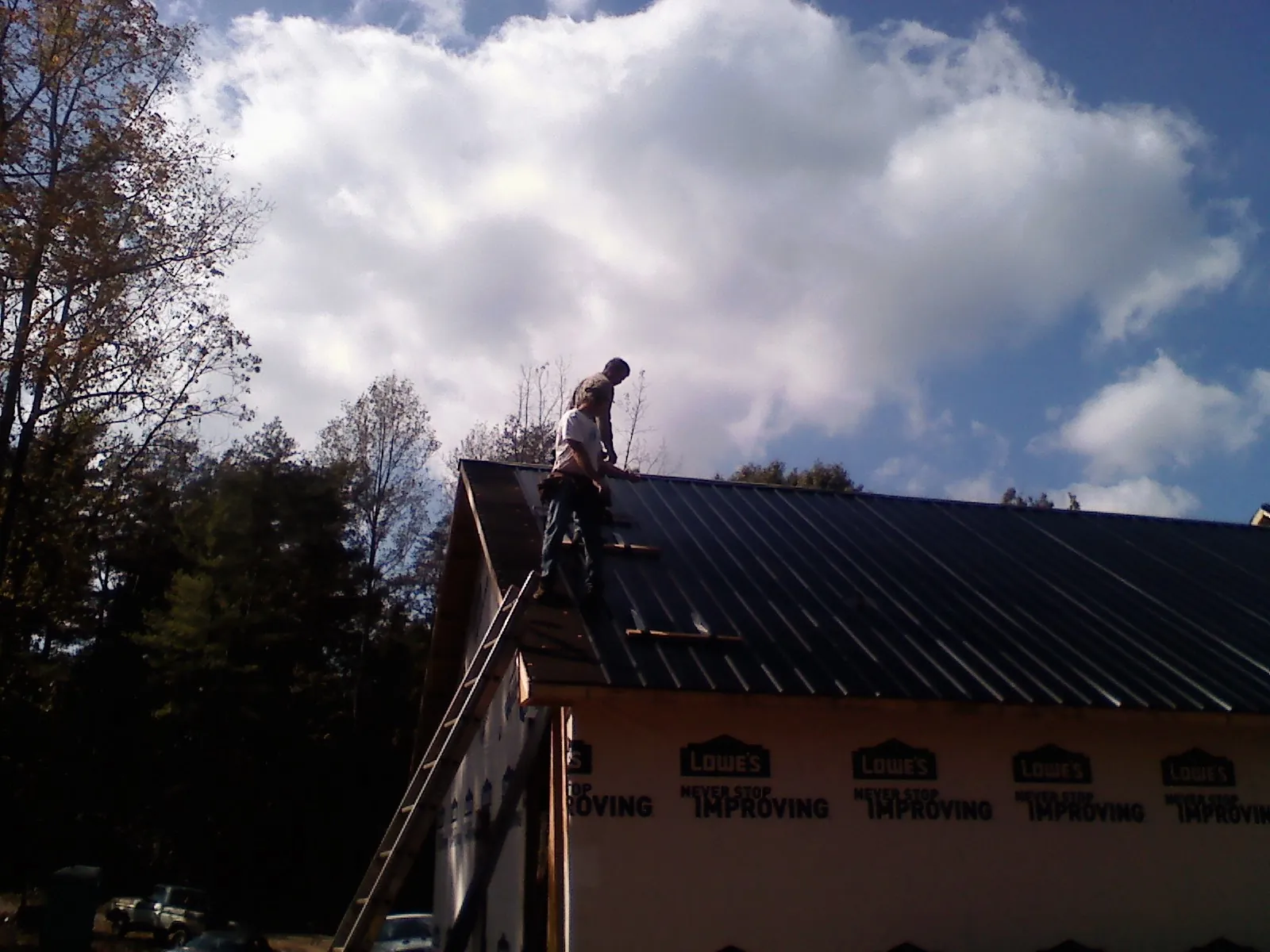 Roofer fastening dark metal panels high against a cloudy sky, from a Roof Inspection job in Cedar Creek