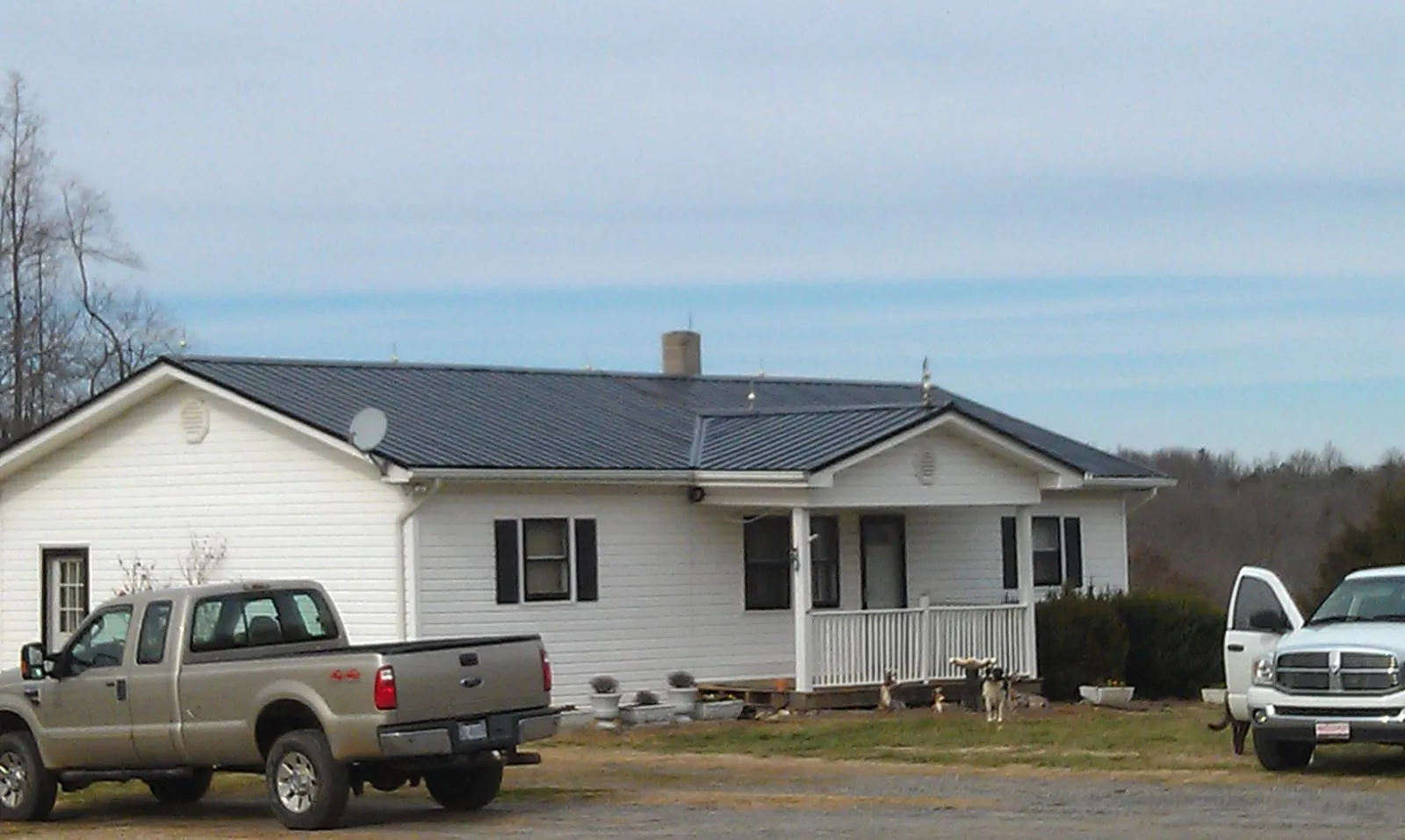 Finished dark metal roof on a white ranch home with work trucks parked in Cedar Creek