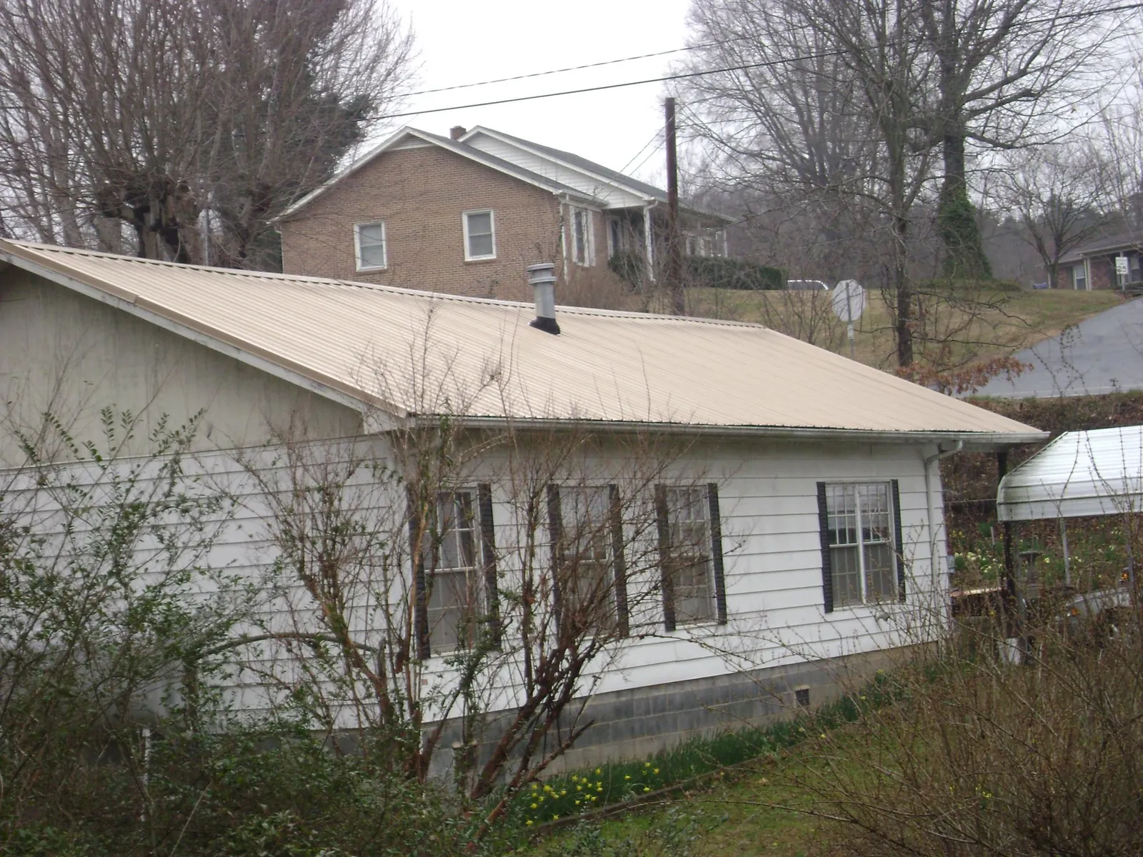 Tan metal roof on a white sided house set into a hillside — Commercial Roofing by Roofing Brothers in Cedar Creek